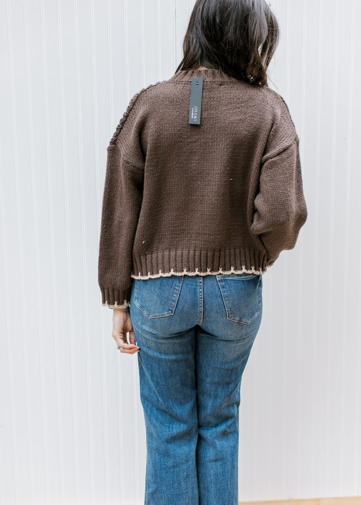 Back view of Model wearing a chunky knit brown sweater with tan stitching and long sleeves. 
