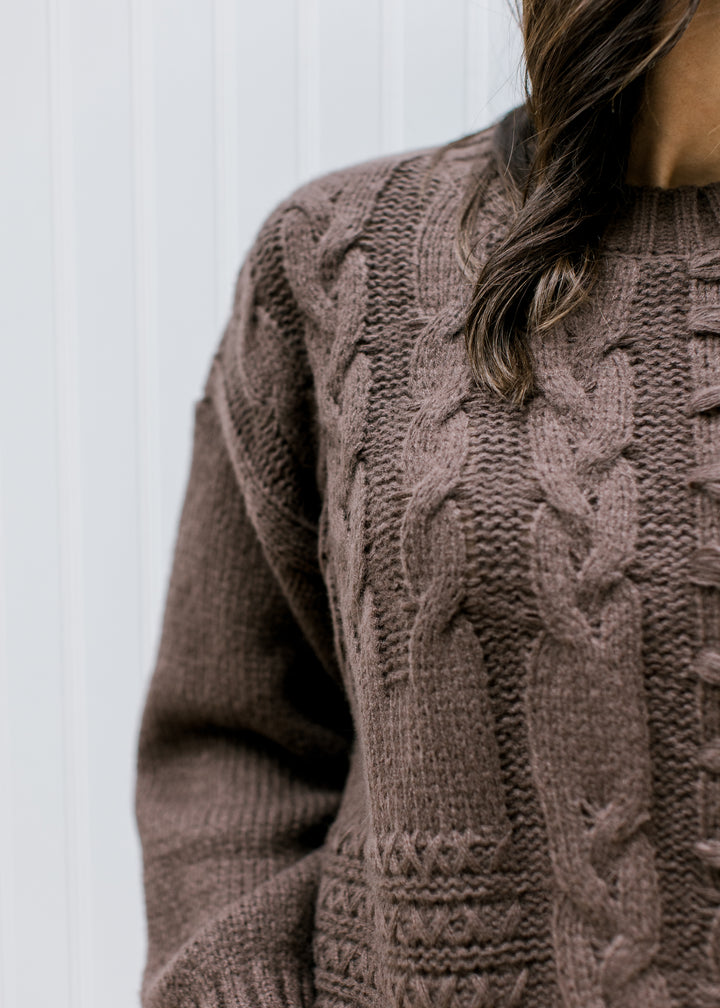 Close up of cable knit texturing on a brown sweater with bubble long sleeves and a round neck.