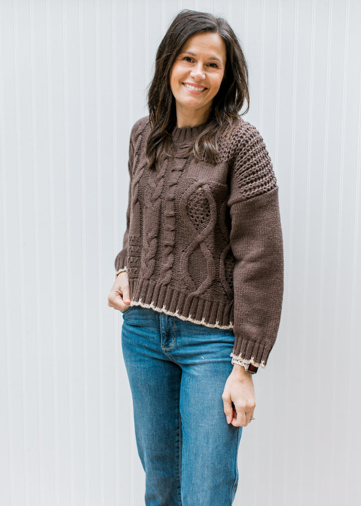 Model wearing a chunky knit brown sweater with tan stitching, long sleeves and a round neck.