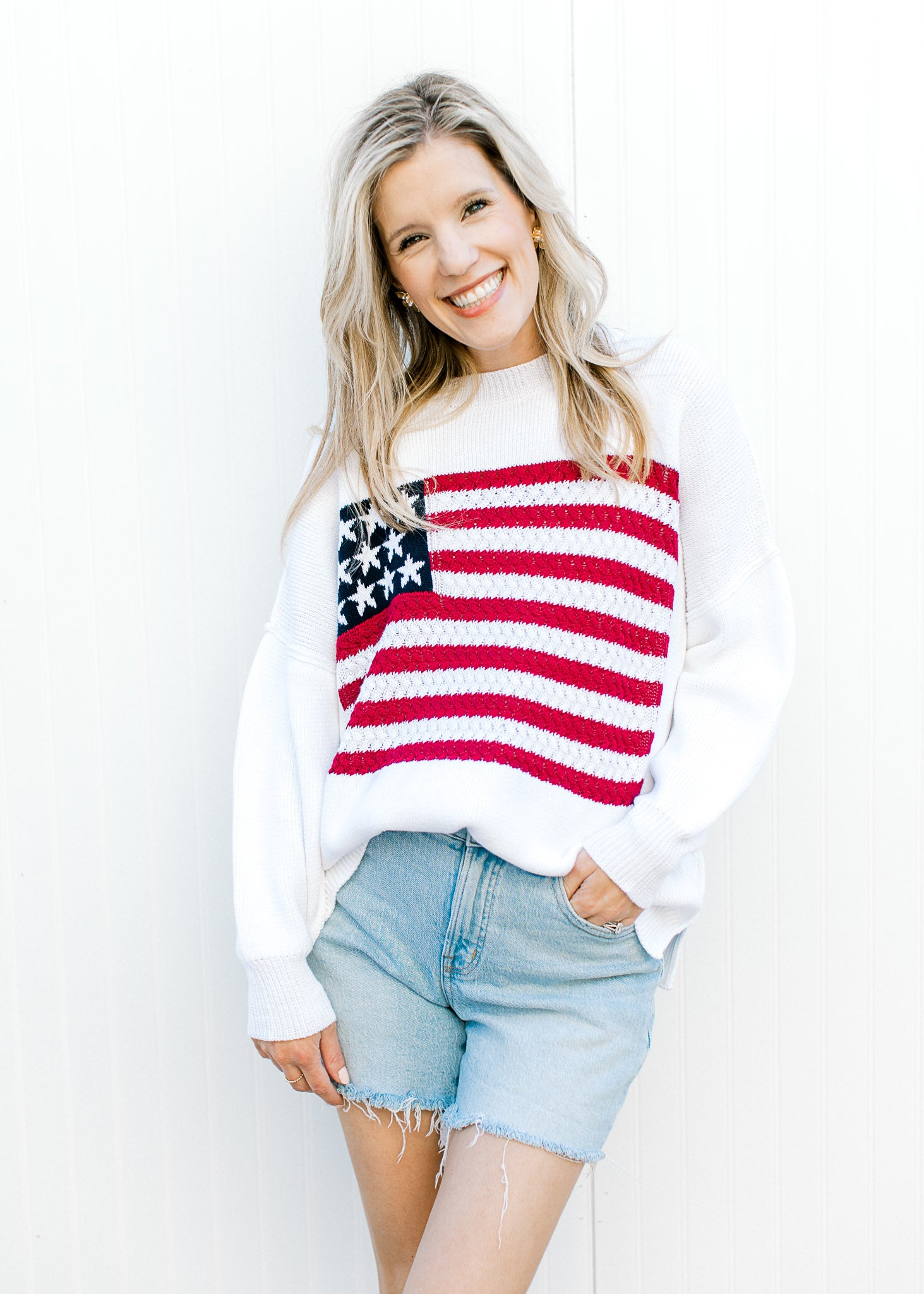 Model wearing shorts and a white knit sweater with a flag pattern, crew neck and long sleeves.