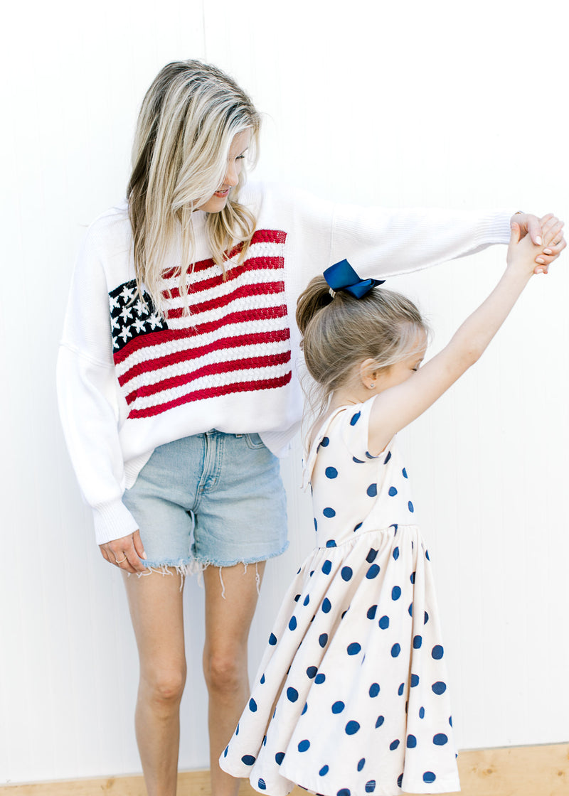 Model with child wearing a white lightweight knit sweater with a flag pattern and long sleeves.
