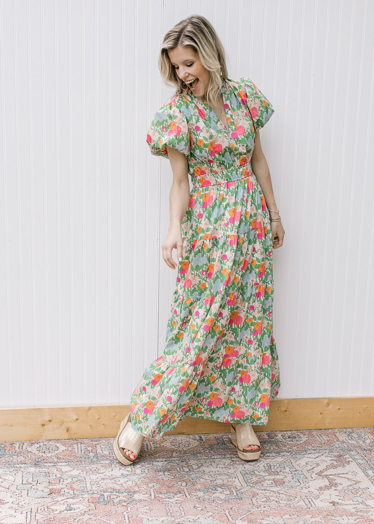 Model wearing wedges and a bright floral maxi with short puff sleeves, elastic waist and a v-neck. 