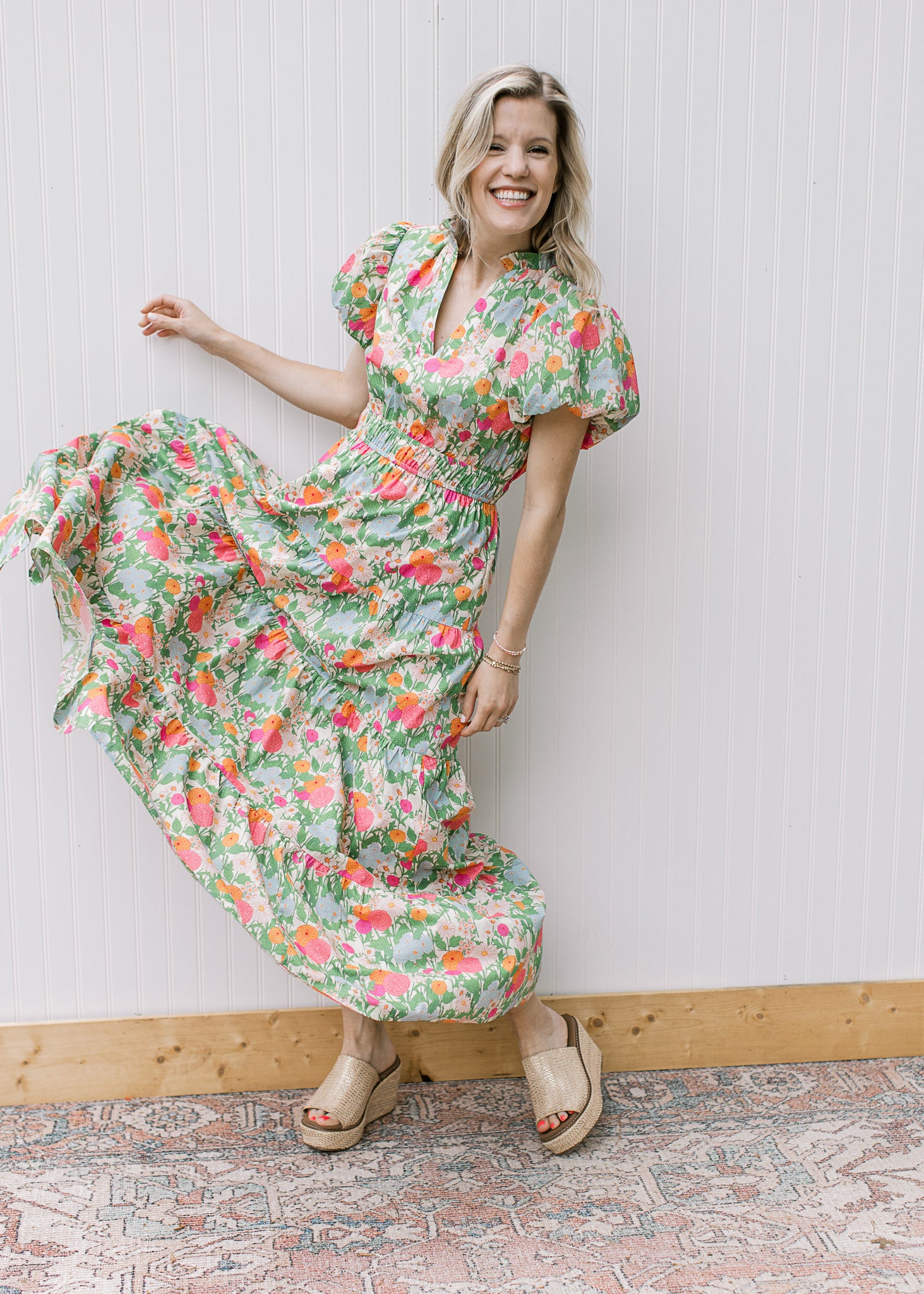 Model wearing a bright, flowy floral maxi with short puff sleeves, elastic waist and a v-neck. 