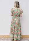 Back view of Model wearing a bright floral maxi with short sleeves, elastic waist and ruffle neck.
