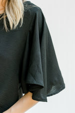 Close up view of flutter short sleeves on a black polyester top with a round neckline. 