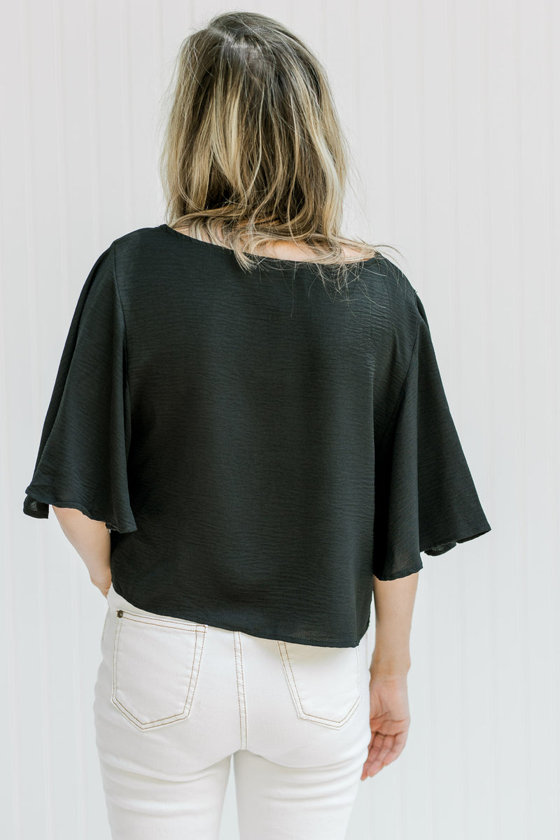 Back view of a model wearing a black cropped top with flutter short sleeves and a round neckline. 