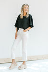 Model wearing white jeans with a black cropped top with flutter short sleeves. 