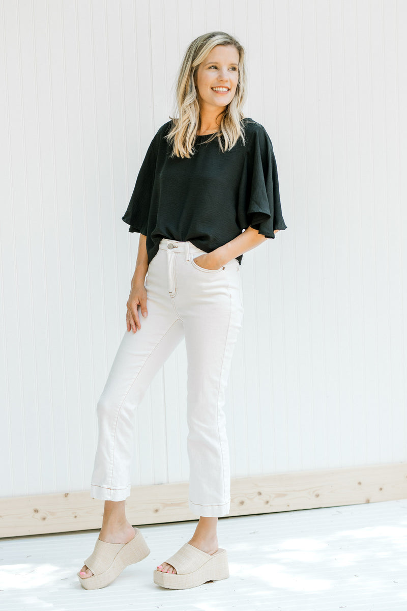 Model wearing white jeans with a black cropped top with flutter short sleeves. 