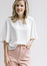 Model wearing an ivory polyester slightly cropped top with flutter short sleeves. 