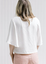 Back view of Model wearing an ivory polyester slightly cropped top with flutter short sleeves. 
