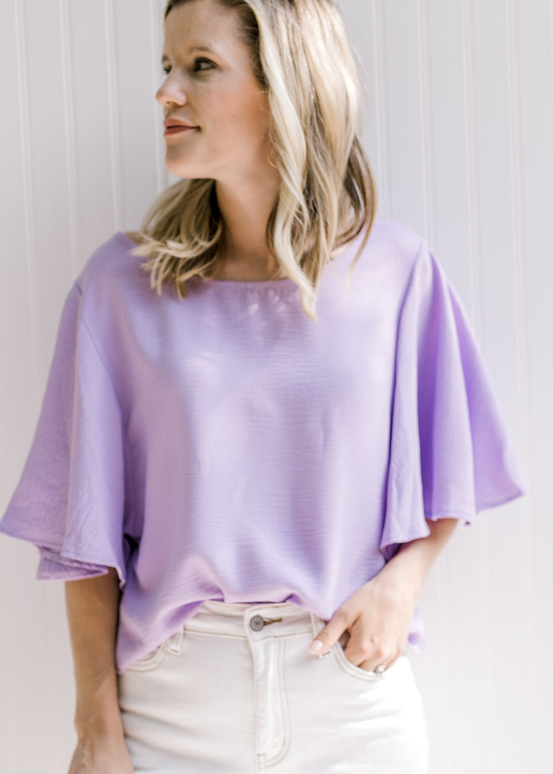 Model wearing a light lavender slightly cropped top with flutter short sleeves. 