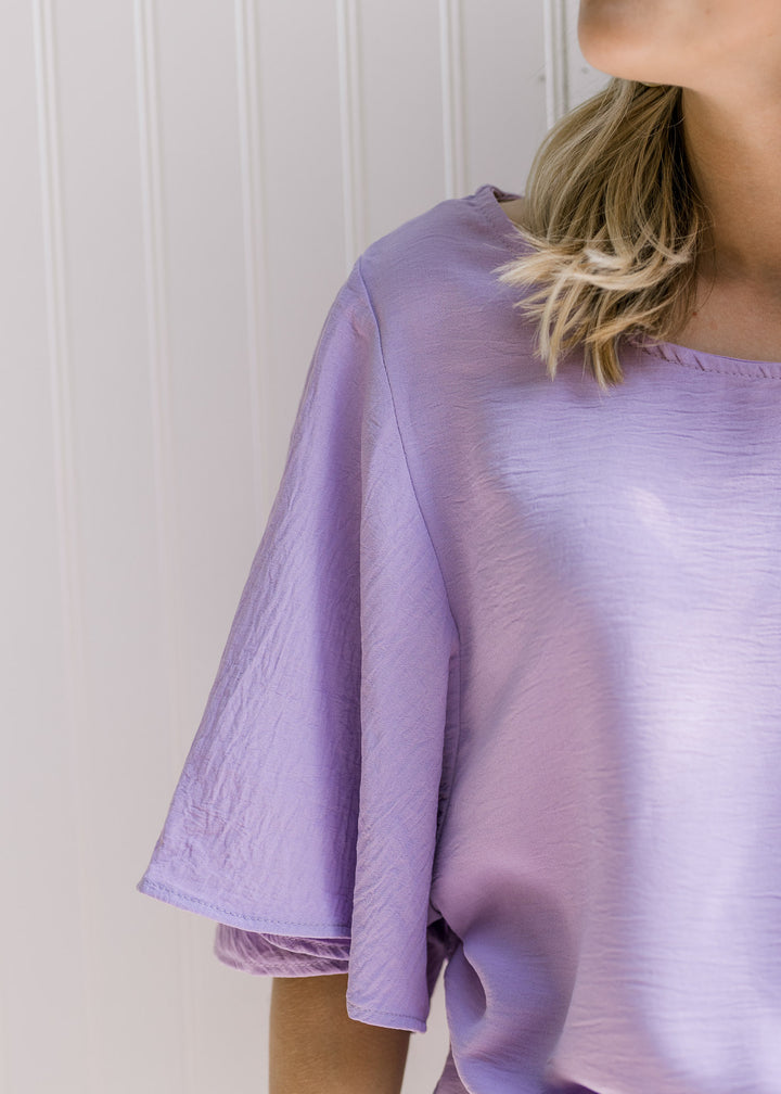 Close up of flutter short sleeves on a lavender top that is slightly cropped. 