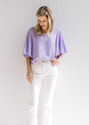 Model wearing white jeans with a lavender slightly cropped top with a round neck and short sleeves. 