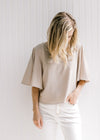 Model wearing a polyester taupe crop top with flutter short sleeves and a flowy fit. 