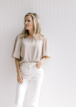 Model wearing white jeans with a taupe crop top with flutter short sleeves and a flowy fit. 
