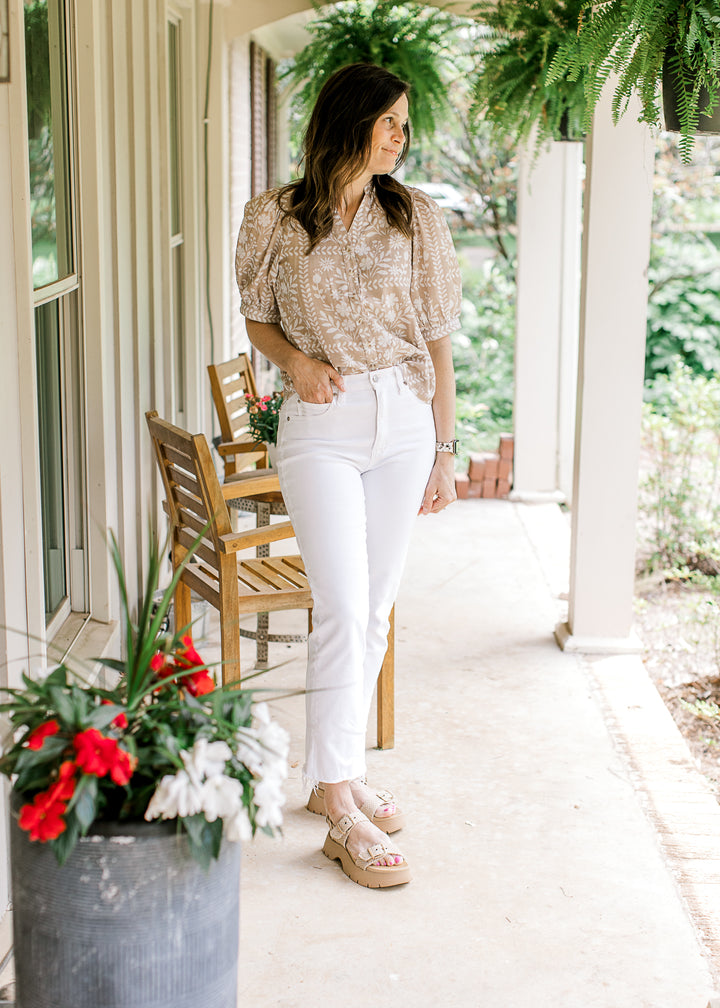 Model wearing white jeans and a wheat top with white floral, short sleeves and  v-neck with buttons.