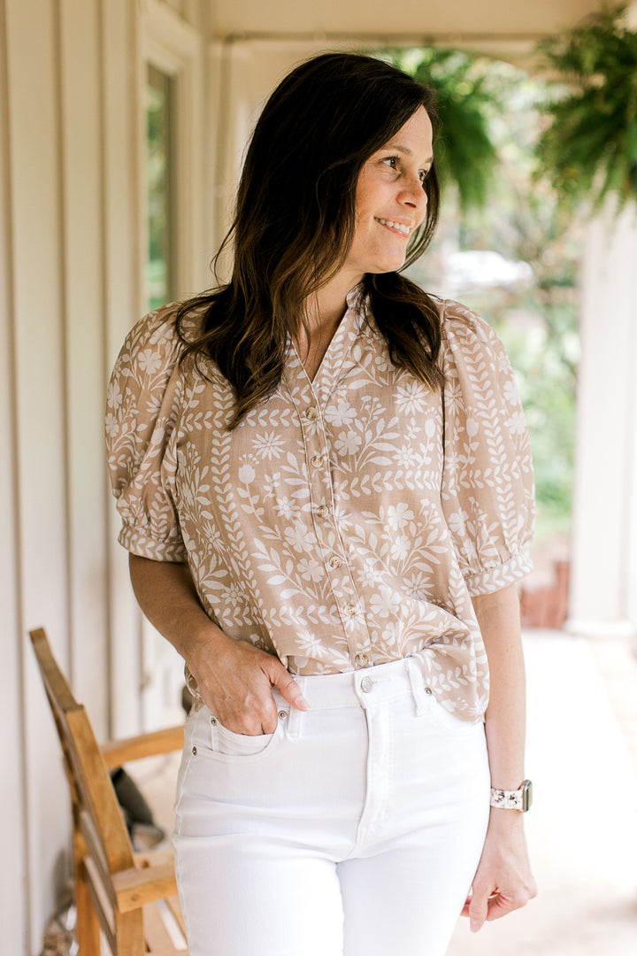 Model wearing a wheat top with white floral, short sleeves and  v-neck with buttons.
