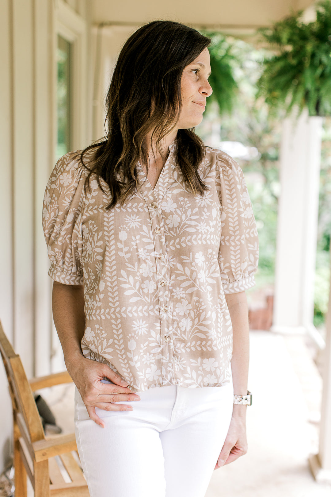 Model wearing a button up wheat colored top with white floral, short sleeves and a v-neck. 