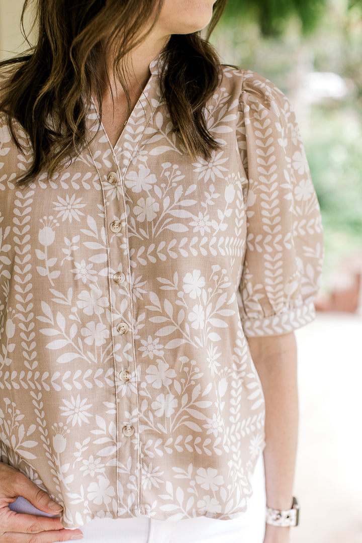 Close up of v-neck and button front on a wheat color top with white flowers and short sleeves.