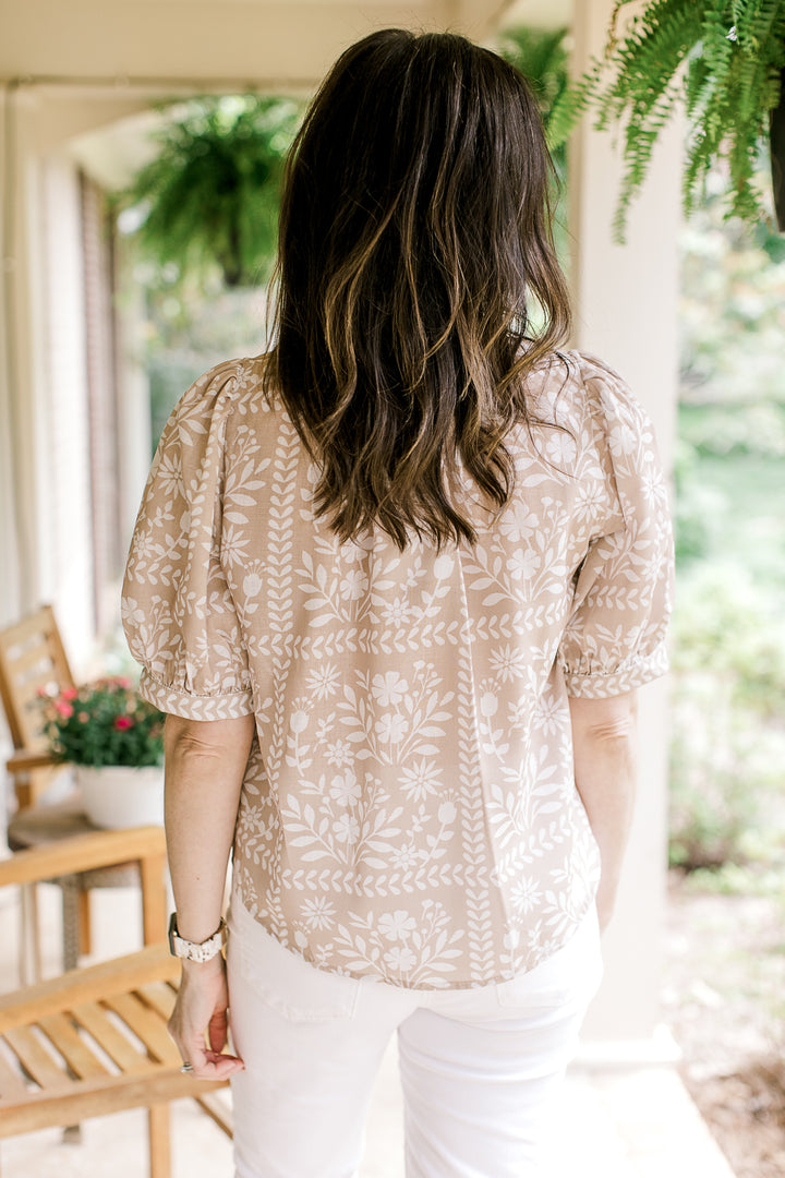 Back view of Model wearing a wheat top with white floral, short sleeves and  v-neck with buttons.