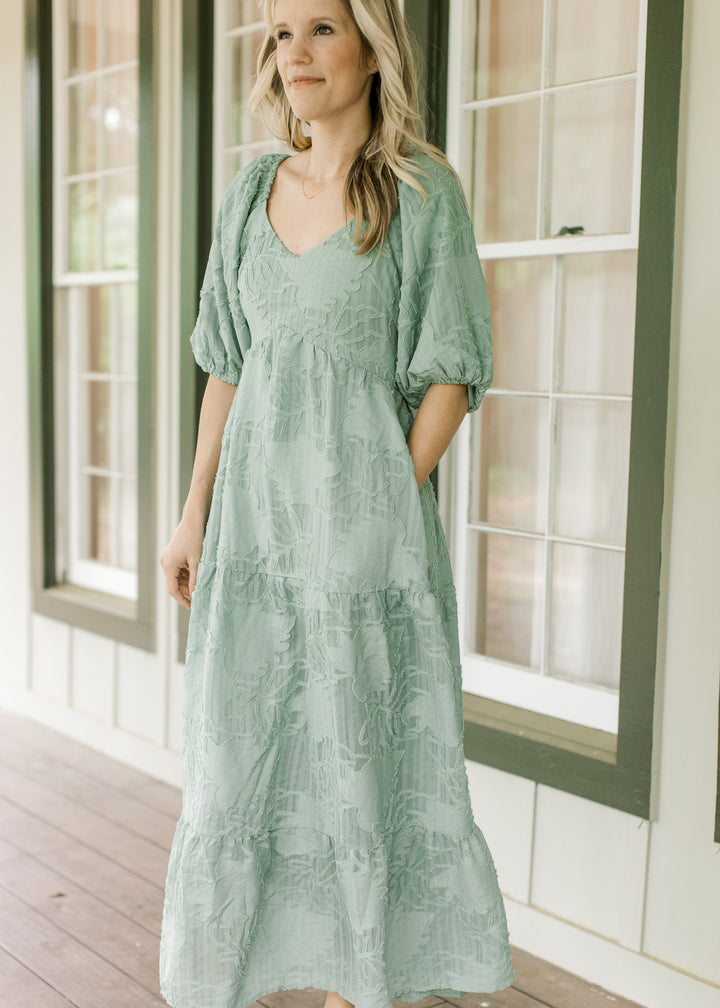 Model wearing a sage midi with textured leaf pattern, v-neck and bubble short sleeves.