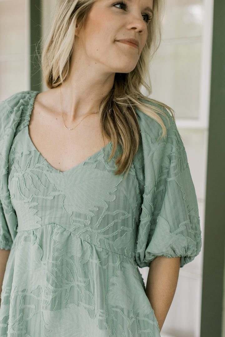 Close up of textured leaves and a v-neck on a sage midi with bubble short sleeves. 