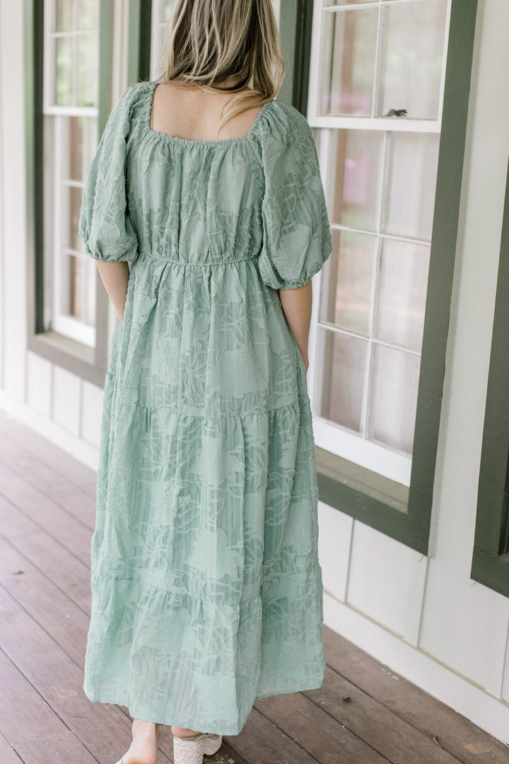Back view of Model wearing a sage midi with textured leaf pattern, v-neck and bubble short sleeves.