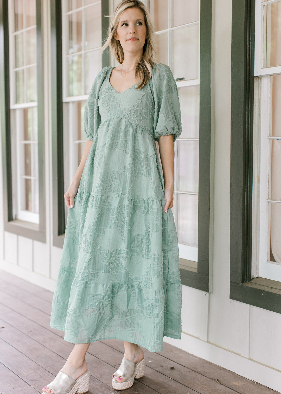 Model wearing wedges with a sage midi with textured leaf pattern, v-neck and bubble short sleeves. 