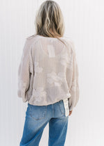 Back view of Model wearing an oatmeal sweater with stitched flowers and bubble long sleeves.