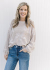 Model wearing an oatmeal colored knit sweater with stitched flowers and bubble long sleeves.