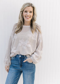 Model wearing an oatmeal colored knit sweater with stitched flowers and bubble long sleeves.