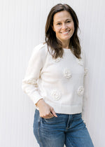 Model wearing a cream sweater with appliqué flowers, long sleeves and pleated shoulders. 