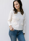 Model wearing a cream sweater with appliqué flowers, long sleeves and ribbed cuff, neck and hem.