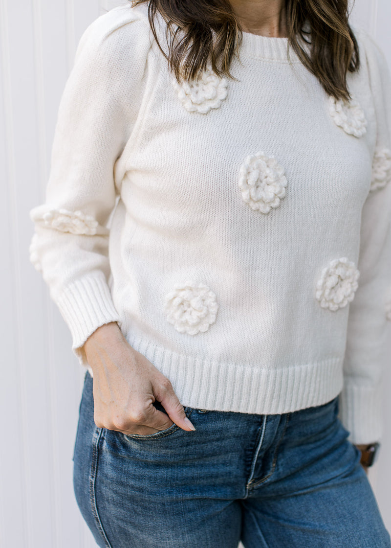 Close up of appliqué flowers pleated shoulders on a cream sweater with long sleeves. 