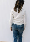 Back view of Model wearing a cream sweater with appliqué flowers, long sleeves and pleated shoulder.