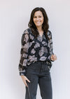Model wearing a black top with a gray floral pattern, sheer long sleeves and v-neck with a tie. 