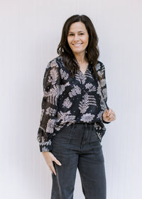 Model wearing a black top with a gray floral pattern, sheer long sleeves and v-neck with a tie. 
