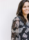 Close up of sheer long sleeves on a black top with gray floral and a v-neck with a ruffle and a tie.