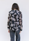 Back view of Model wearing a black top with a gray floral pattern, sheer long sleeves and a v-neck