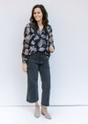 Model wearing jeans with booties and a black top with a gray floral pattern and sheer long sleeves. 