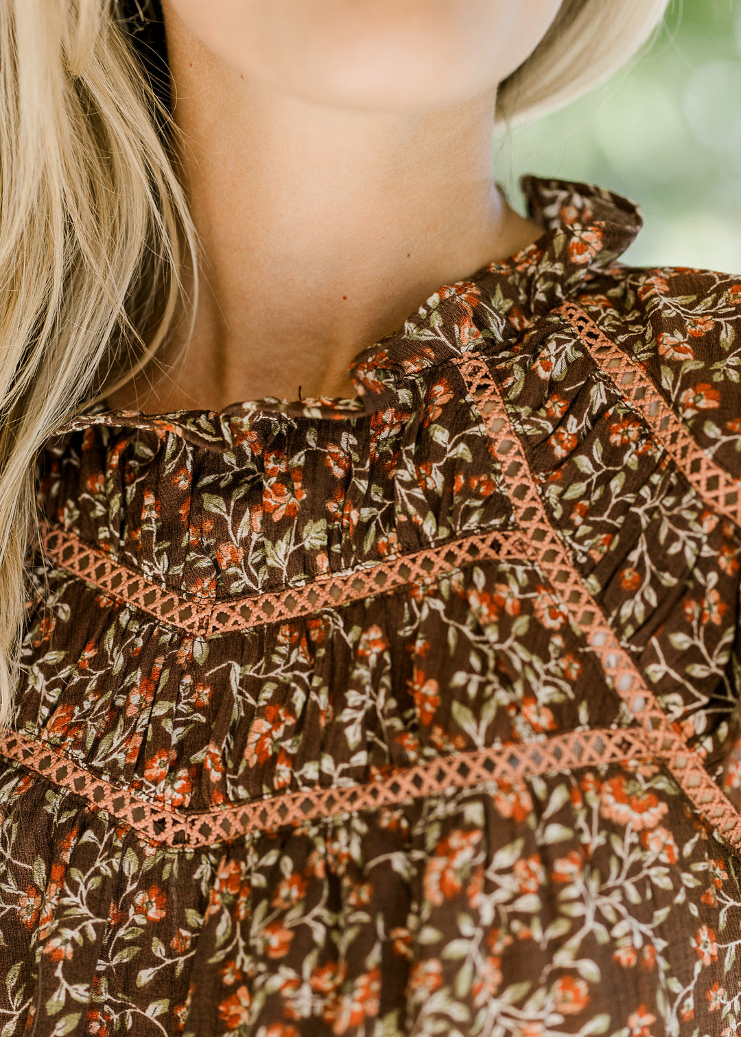 Close up view of ruffle neck and lace at bodice of a brown top with maroon and green floral. 