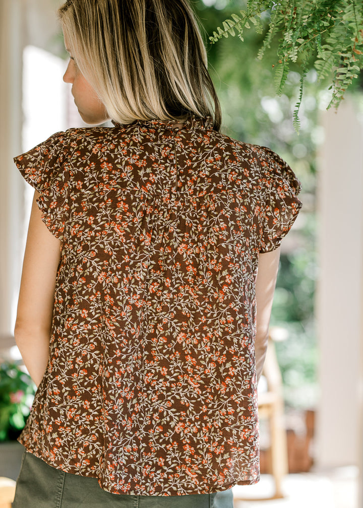 Back view of Model wearing a brown top with maroon and green flora and flutter cap sleeves.