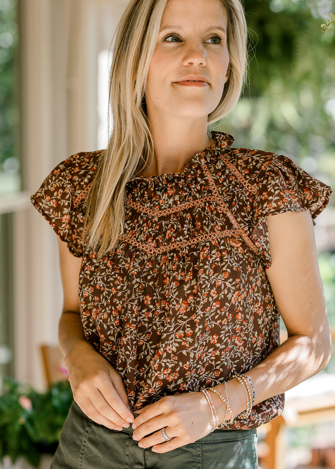 Model wearing a lightweight brown top with maroon and green floral and flutter cap sleeves. 