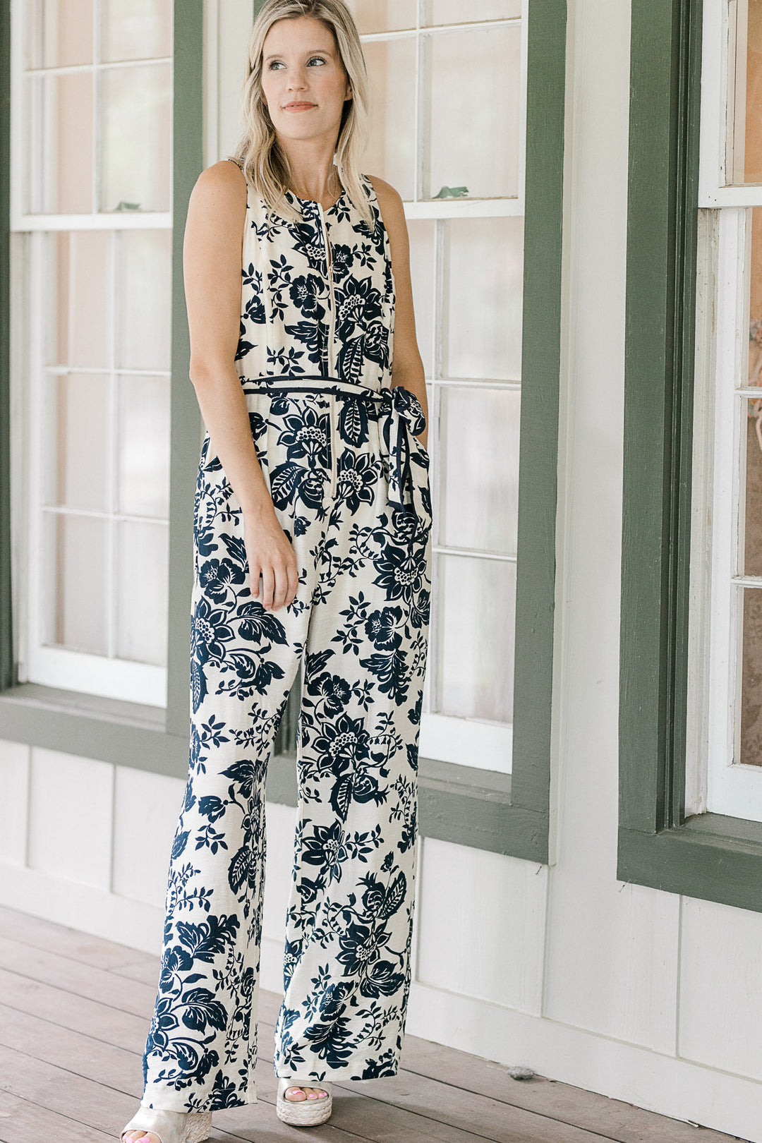 Model wearing wedges and a cream jumper with navy floral, half zipper, pockets and tie at waist. 