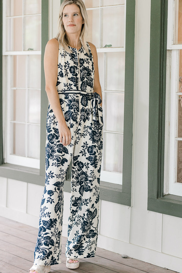 Model wearing wedges and a cream jumper with navy floral, half zipper, pockets and tie at waist. 