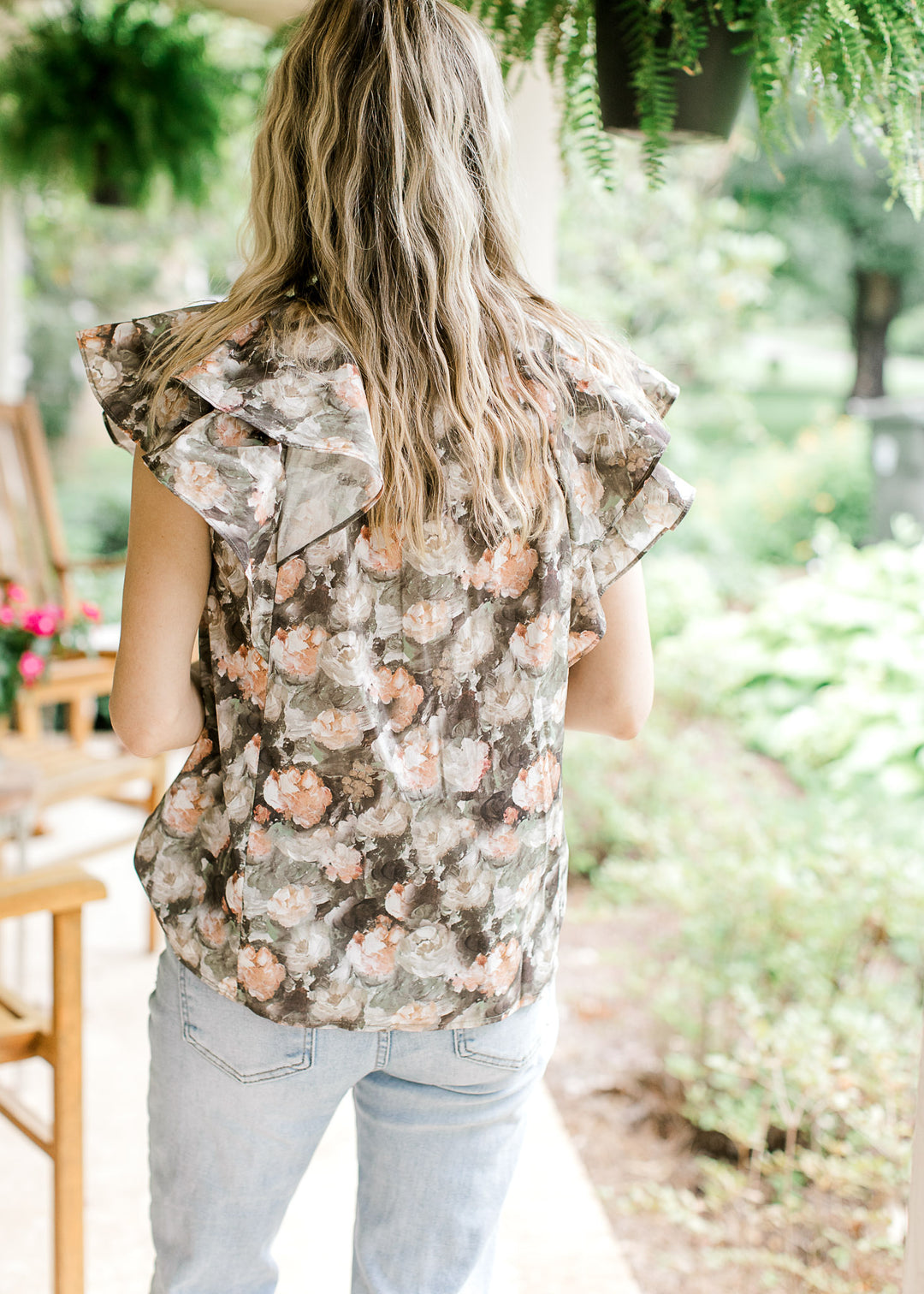 Back view of Model wearing a charcoal top with pink and tan flowers and a double ruffle cap sleeves.