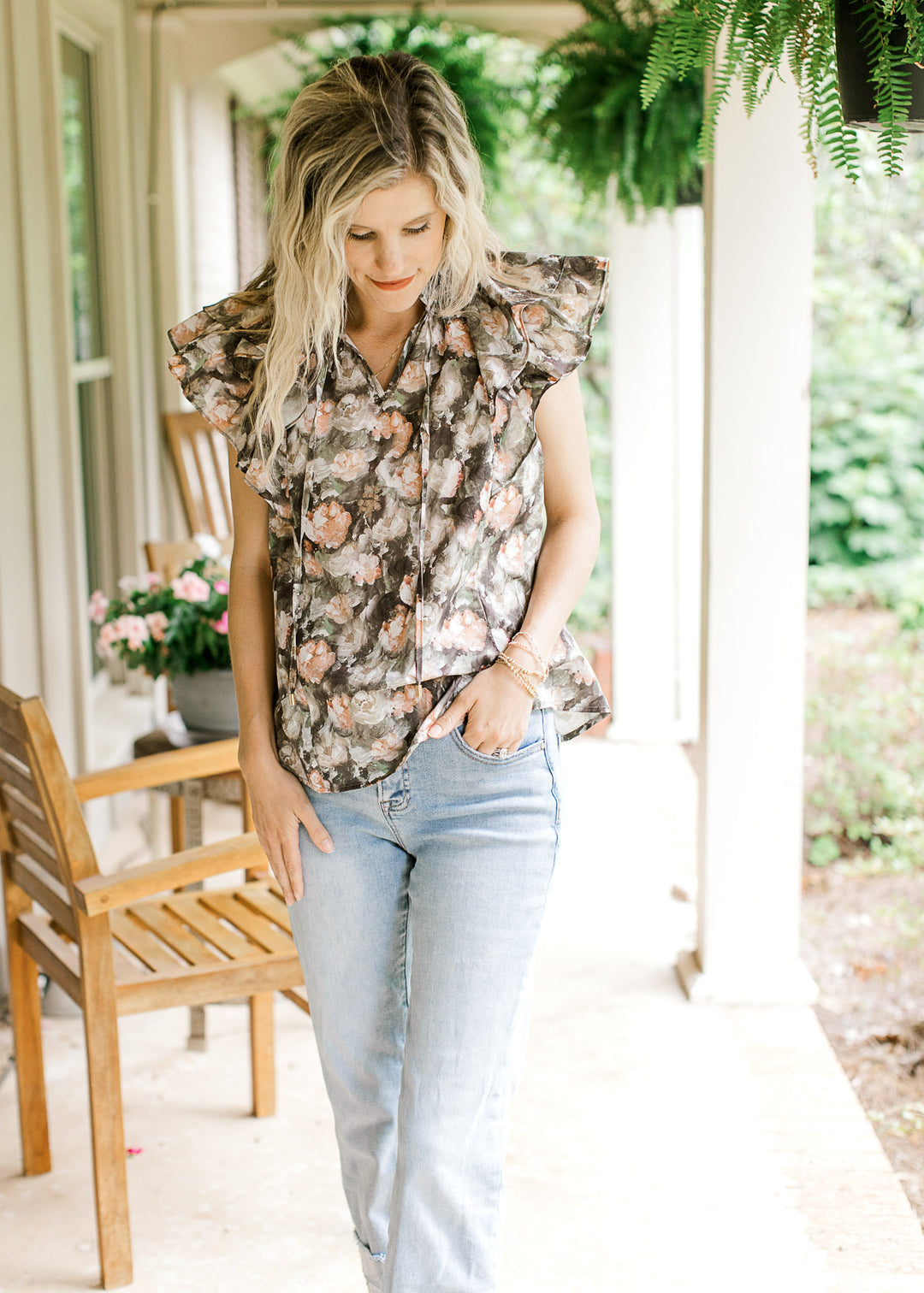 Model wearing a charcoal top with pink and tan oil painted flowers and a double ruffle cap sleeves.