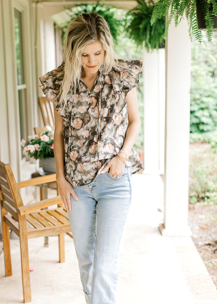 Model wearing a charcoal top with pink and tan oil painted flowers and a double ruffle cap sleeves.