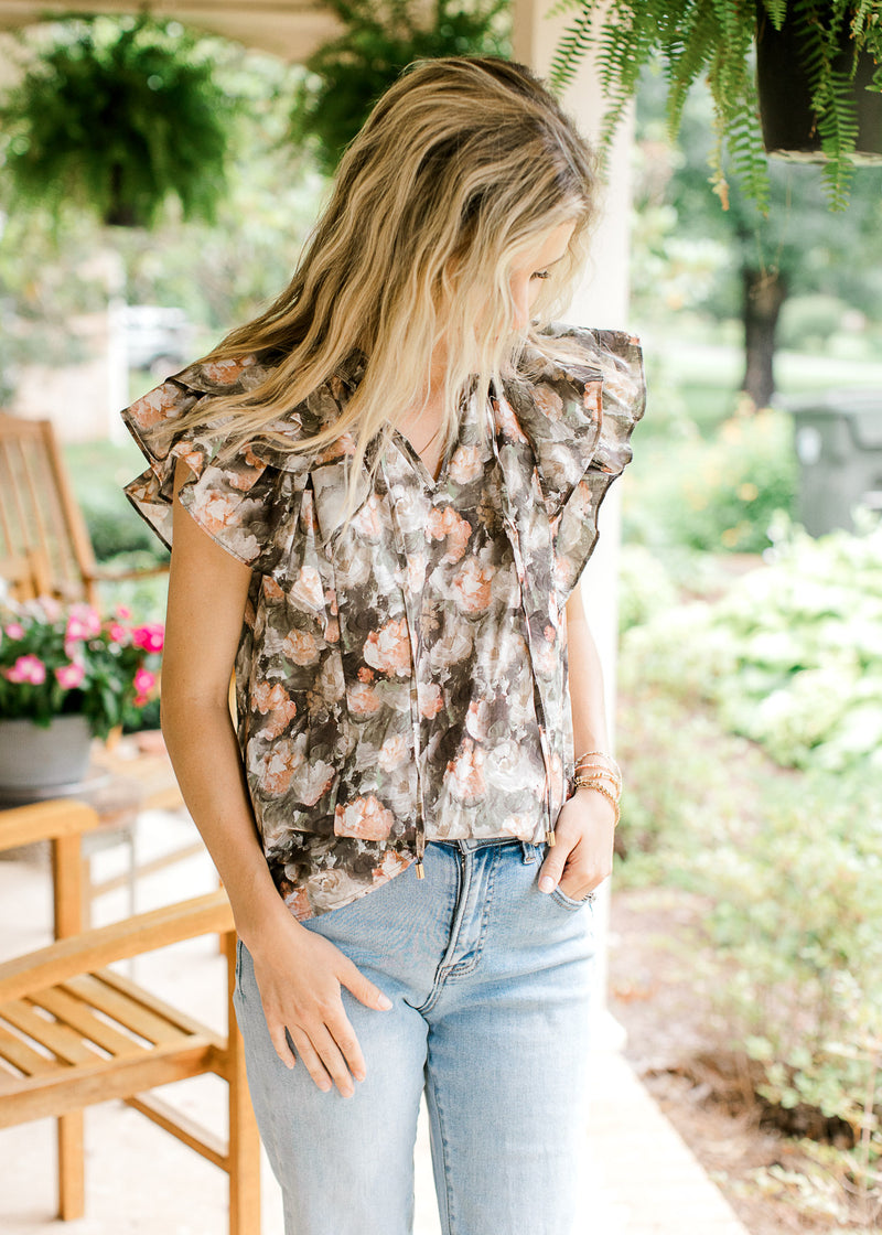 Model wearing a charcoal top with pink and tan painted flowers and a double ruffle cap sleeves.