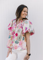 Model wearing a cream top with watercolor floral, a smocked yolk and short bubble sleeves.